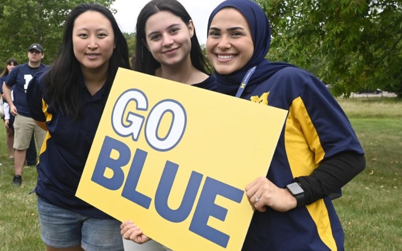 Three female students smiling and holding a poster