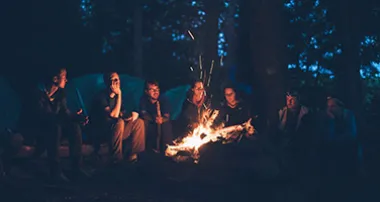 Group of people sitting around a campfire at night