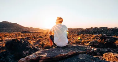 Man sitting and watching the sunset on top of a rock