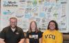 Three people in front of work board and smiling